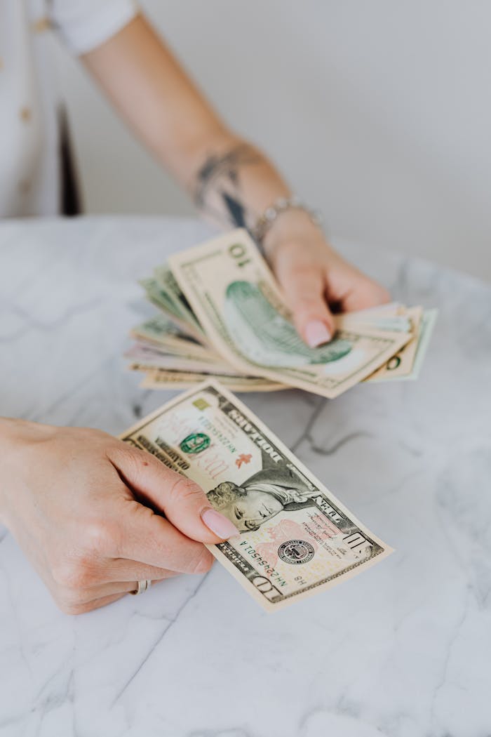 Offres Close-up of hands counting US dollar bills on a marble table, symbolizing personal finance.
